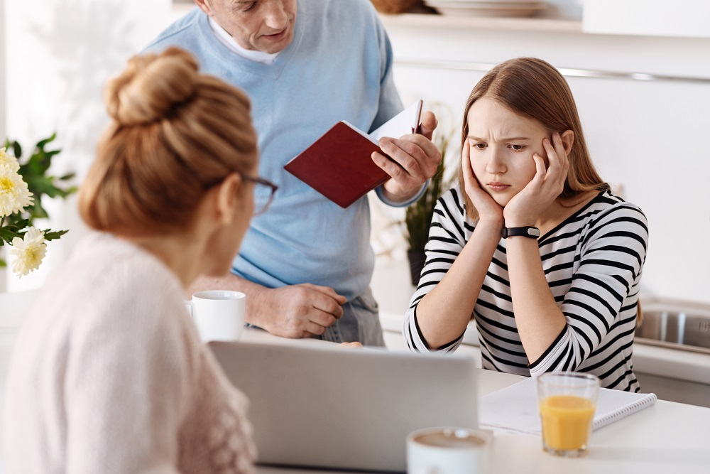 Soziale Medien_Eltern sitzen mit genervtem Mädchen an Tisch