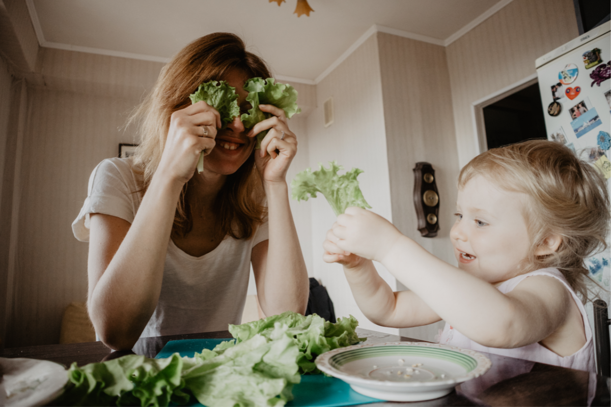 ADHS Kind: Mutter und Kleinkind spiele mit Salat am Esstisch