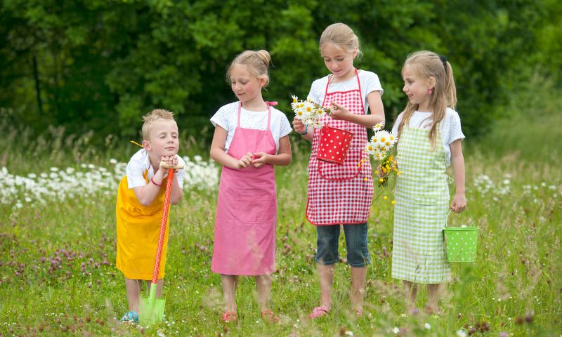Gärtnern mit Kindern: vier Kinder mit Schaufeln und Eimern auf Blumenwiese