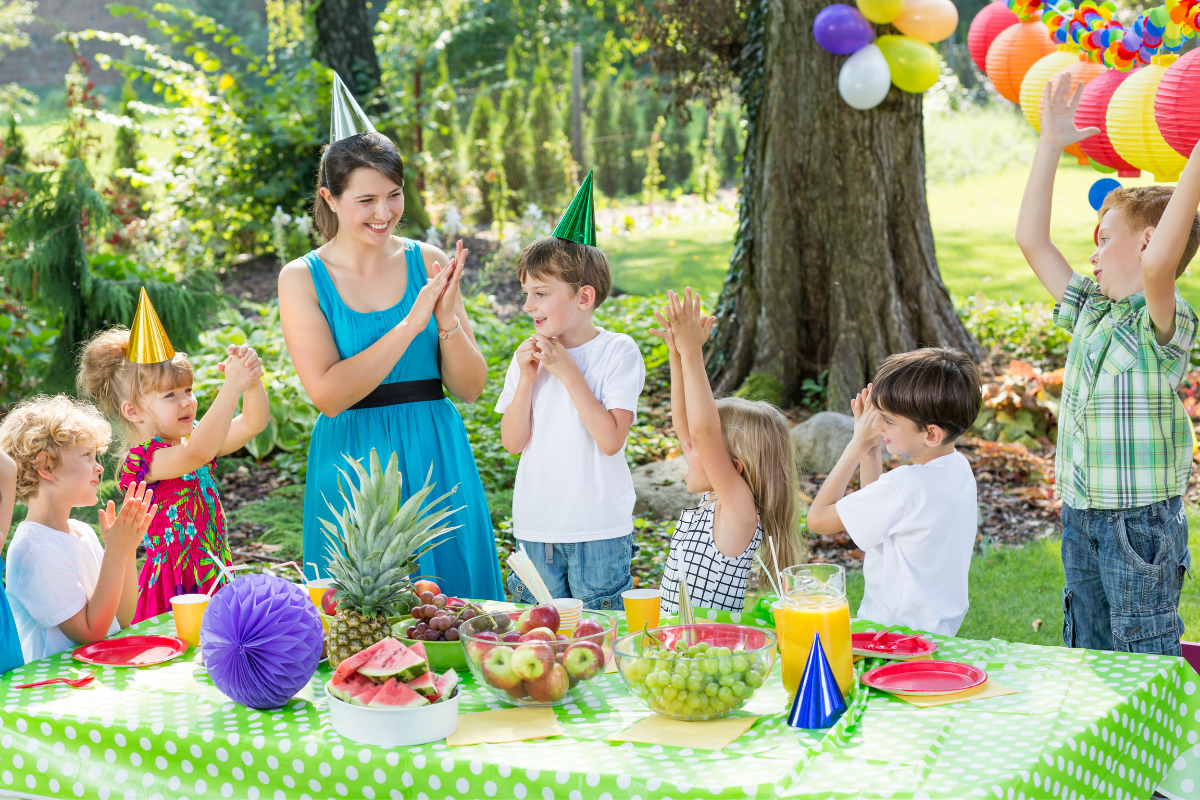 Kindergeburtstag-Idee: Kinder feiern draußen Geburtstag mit Partyhütchen und Essen