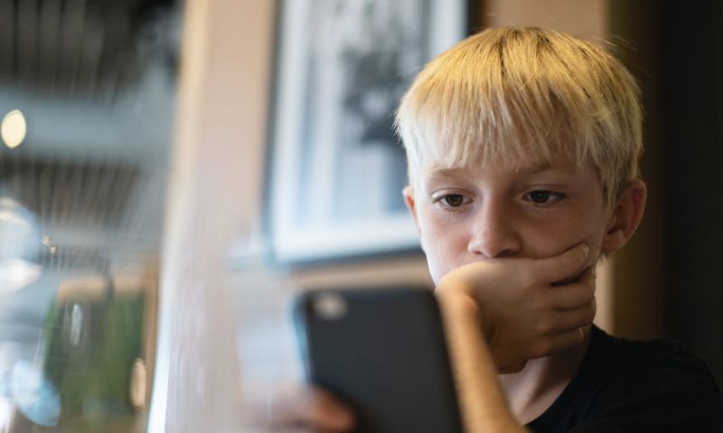 Soziale Medien und Kinder: Junge schaut nachdenklich auf Smartphone