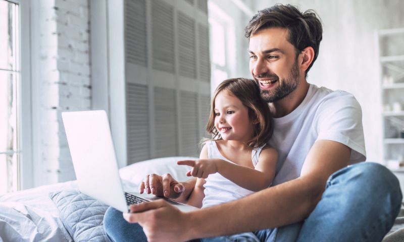 Soziale Medien und Kinder: Vater schaut mit Tochter strahlend auf Laptop