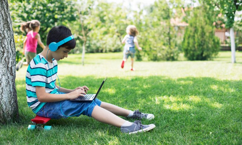 Stubenhocker: Junge mit Kopfhörern und Laptop sitzt auf Wiese