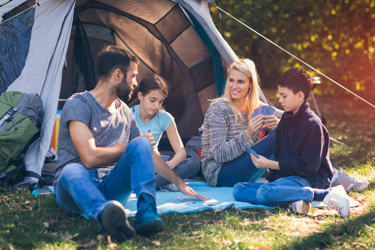 Urlaub am See: Eltern und Kinder spielen Karten vor einem Zelt
