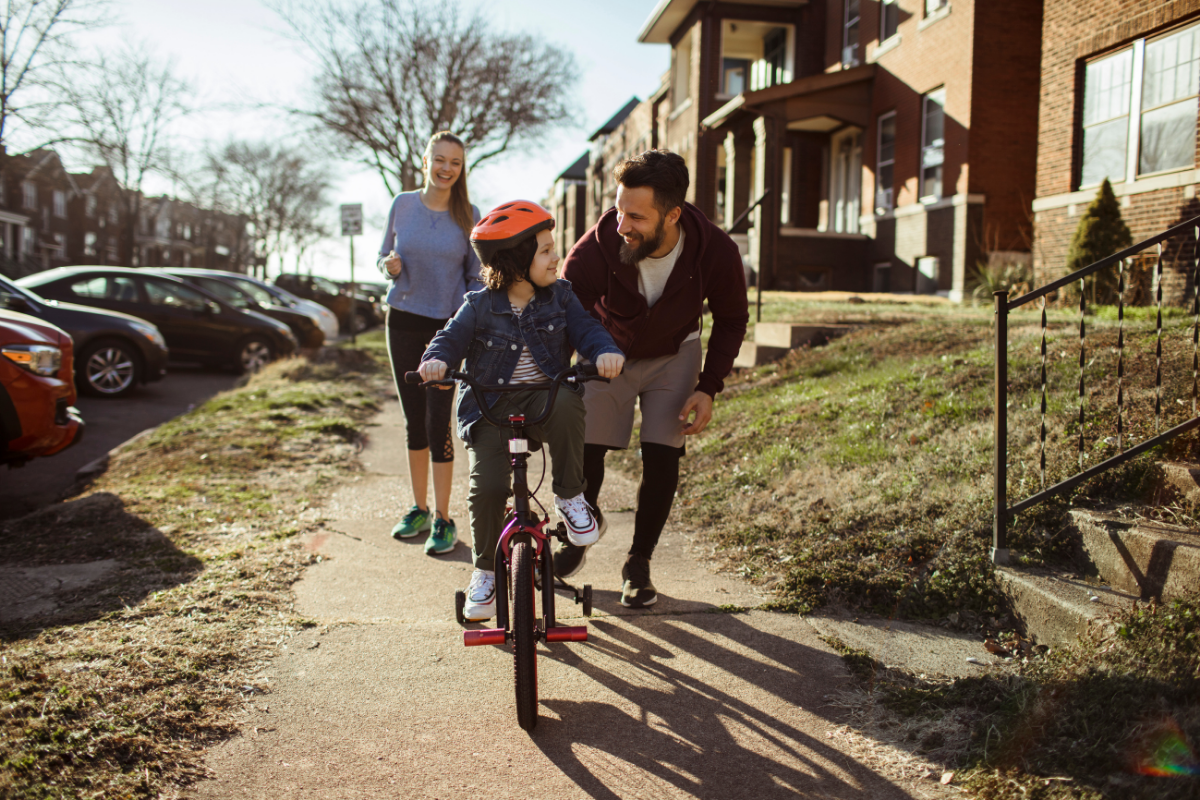 Vorbildfunktion: Kind lernt draußen mit Eltern Fahrrad fahren