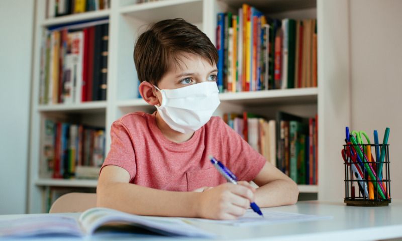 Hygienekonzepte an Schulen: Junge sitzt vor Bücherregal mit Mundschutz