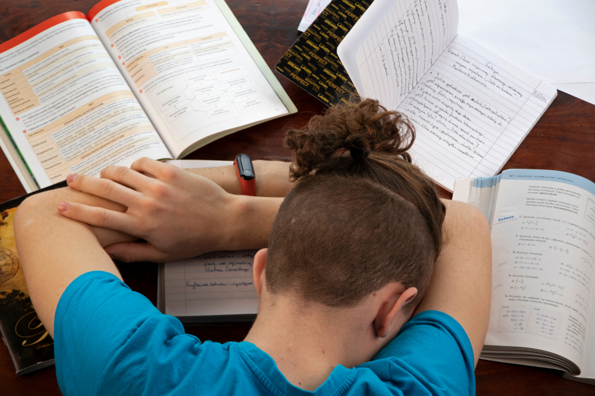 Tipps bei Schulstress: Junge schlaeft erschoepft ueber Hausaufgaben ein