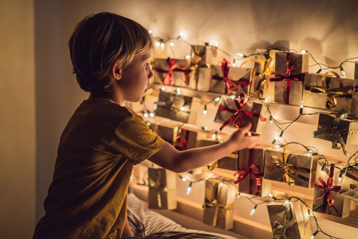 Adventskalender für Kinder_Junge betrachtet Adventskalender, der an Lichterkette hängt