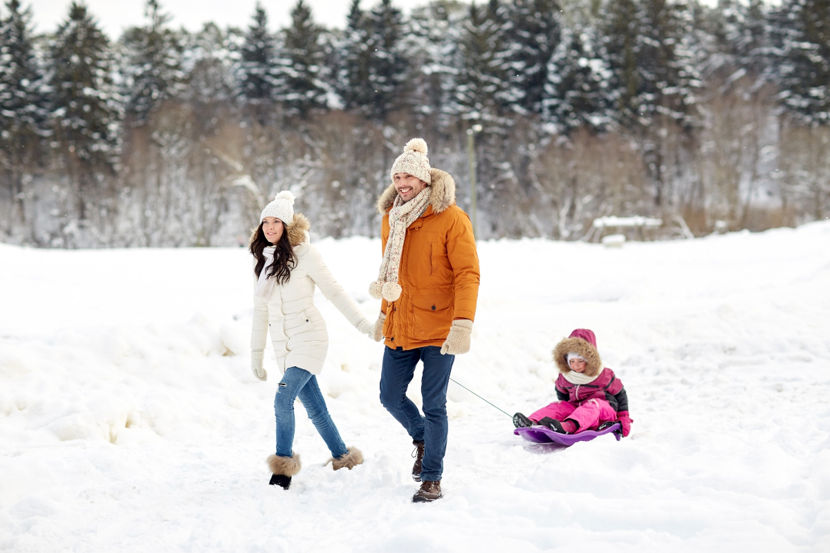 Vorweihnachtszeit Familien-Aktivitäten_Familie unternimmt Winterspaziergang und Kind ist auf Schlitten