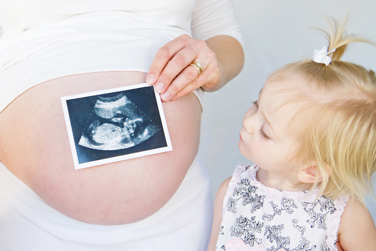 Erstgeborene auf Geschwister vorbereiten_Mutter zeigt Tochter Ultraschallbild vom neuen Geschwisterkind