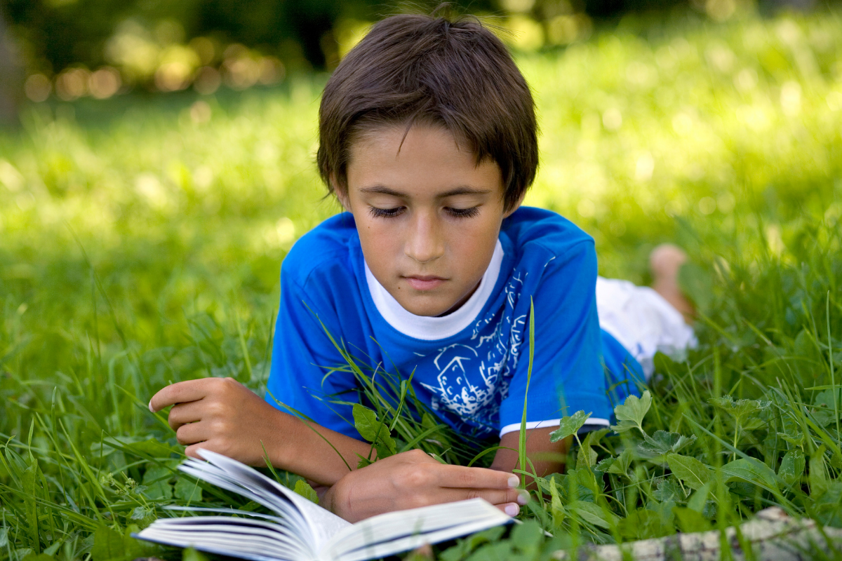 Autismus, Junge liegt im Gras und liest ein Buch