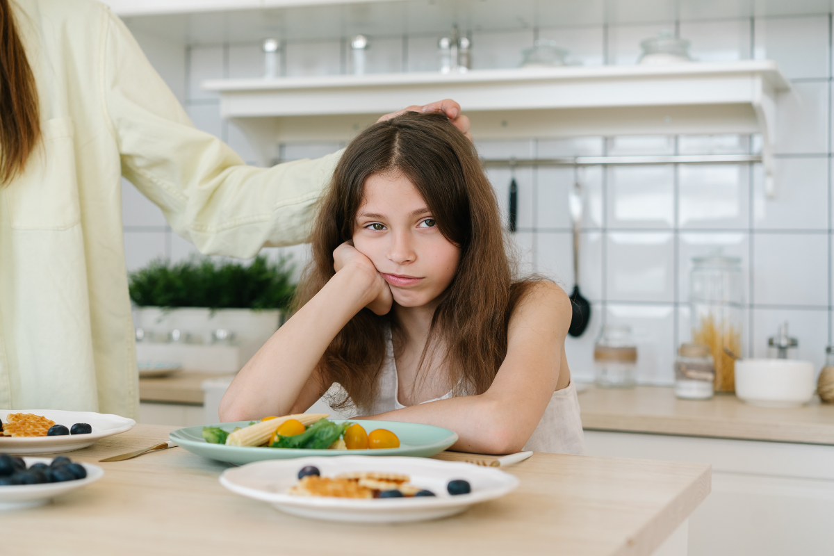 Heimweh nach Mama_Mädchen sitzt am Küchentisch und will nicht essen