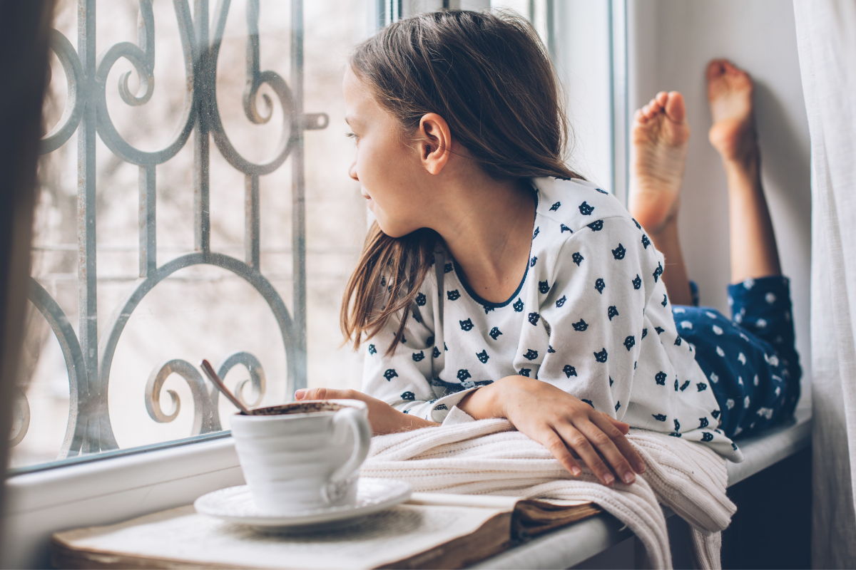 Hypersensibilität bei Kindern_Mädchen macht entspannt Pause und sitzt mit heißem Getränk auf Fensterbank