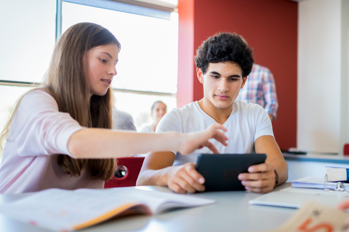 Lernen mit digitalen Medien, Junge und Mädchen im Klassenraum mit Tablet und Büchern