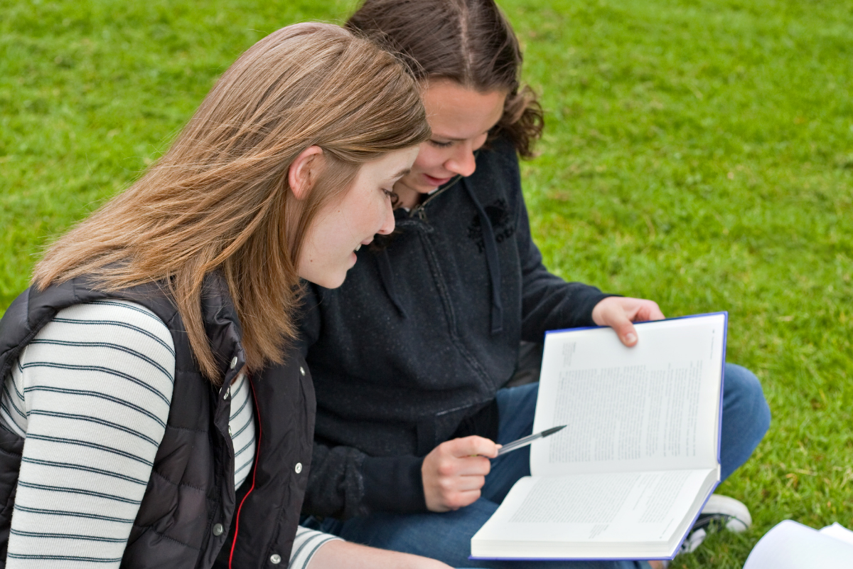 Draußen lernen, 2 Mädchen mit Büchern sitzen im Park
