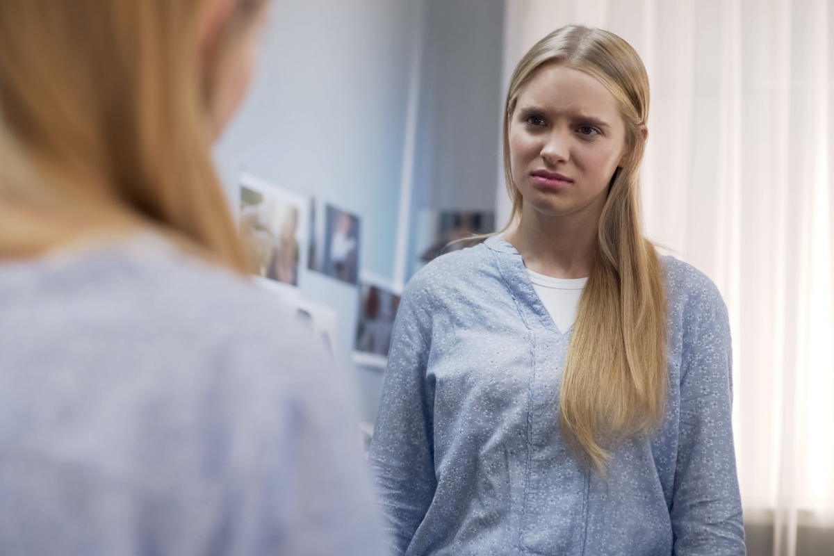 mediale vorbilder, junges mädchen schaut sich zweifelnd im spiegel an