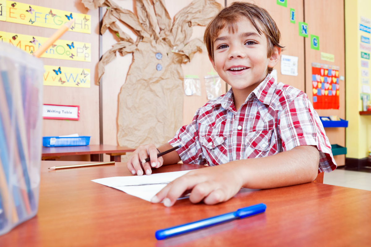 Diktate üben_Schulkind lächelt und schreibt Diktat in Deutsch mit Stift und Schreibheft