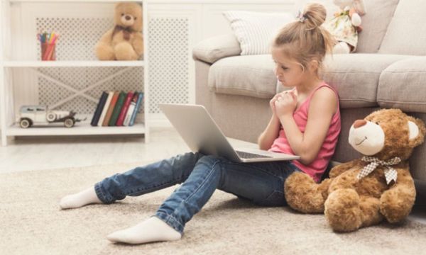 Bildungsgutschein: Mädchen sitzt allein mit Laptop und Teddy in ihrem Kinderzimmer