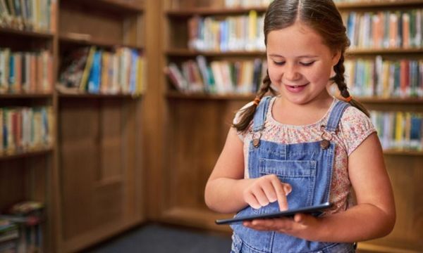 Digitaltag: Mädchen steht mit Tablet in Bibliothek