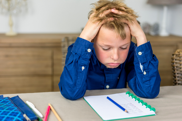 Kind will keine Hausaufgaben machen_Schuljunge sitzt verzweifelt vor den Hausaufgaben