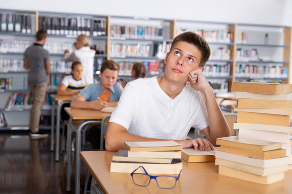 Schulwechsel Realschule Gymnasium, Junge sitzt am Tisch mit Büchern und denkt nach